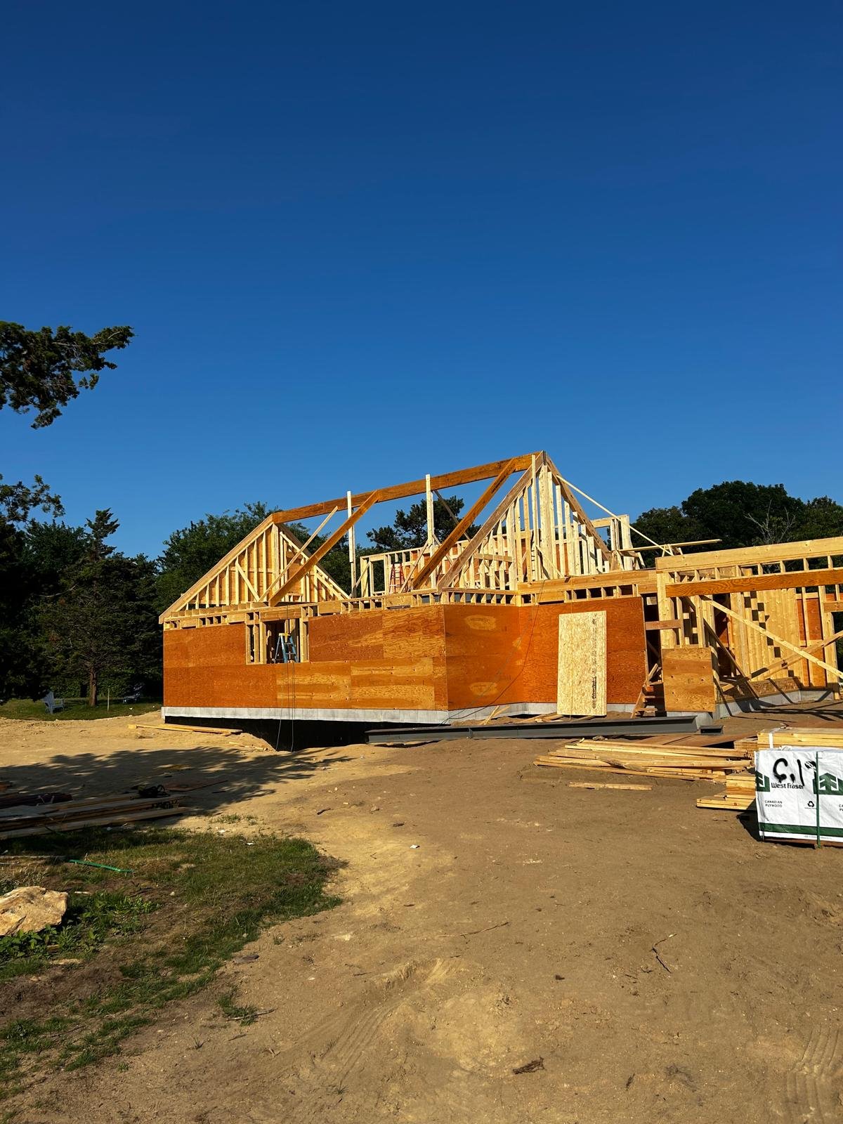 Raw wood framing of a house, rafters, trusses, sheathing and a steel beam over the foundation